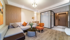 A modern living room with a sectional sofa, a round coffee table, and a small orange armchair. - Kare Hotels (Shenzhen)