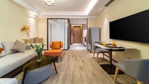 A modern living room with a sofa, coffee table, and chairs, a dining area with a table and chairs, a flat-screen TV, and a kitchen area with a refrigerator. - Kare Hotels (Shenzhen)