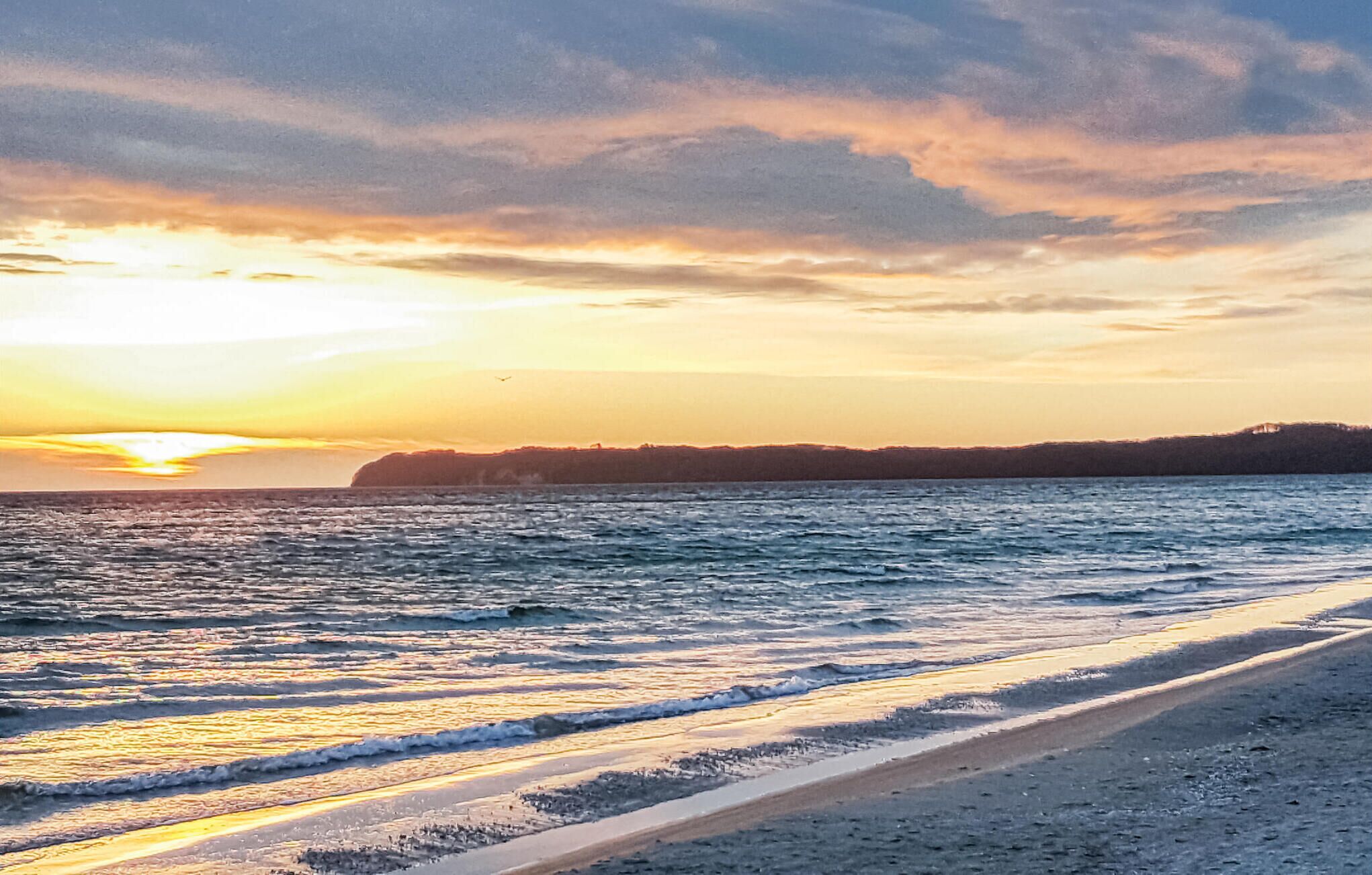 Ein Strand mit Wellen und einem Sonnenuntergang.