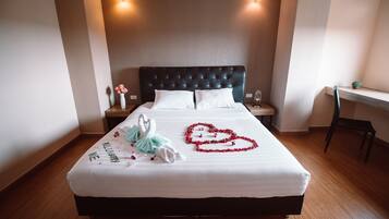 Una cama bien tendida con sábanas blancas, cabecera acolchada y un arreglo floral con forma de corazón sobre el edredón.
