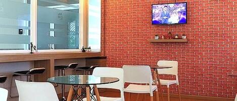 Una habitación moderna con pared de ladrillo, un televisor montado en ella y una mesa de vidrio con sillas blancas.
