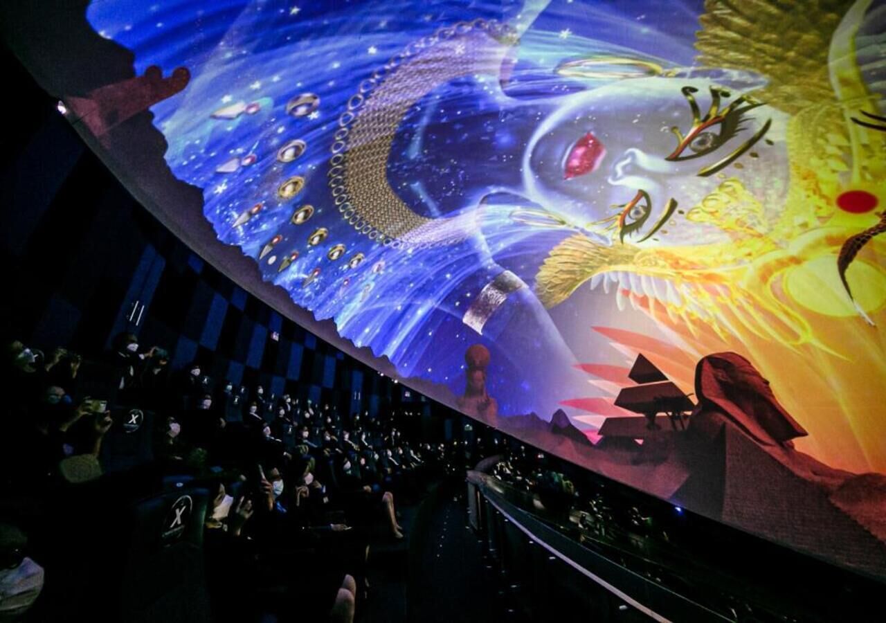 A large, illuminated mural with space-themed artwork, a crowd of people, and a stage area.
