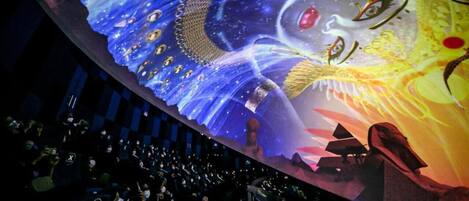 A large, illuminated mural with space-themed artwork, a crowd of people, and a stage area.