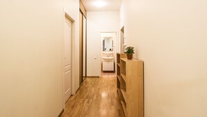 Un couloir étroit au plancher de bois, une porte blanche sur la gauche et un comptoir en bois avec une plante sur la droite.
