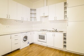 A compact kitchen with white cabinetry, a built-in washing machine, an oven, and a sink.