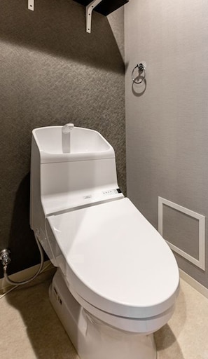 A white toilet in a bathroom with a grey wall and a black shelf above it.