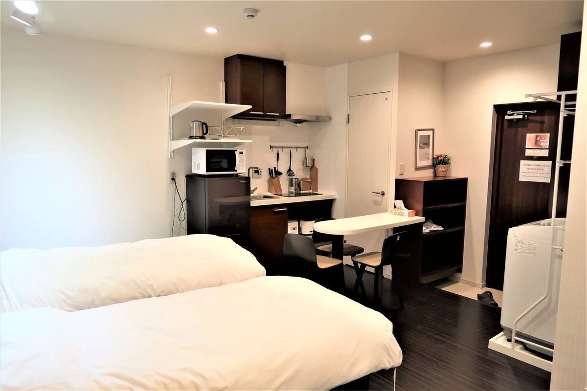 Quarto de hotel compacto com cozinha compacta, duas camas, uma mesa de jantar e um frigorífico pequeno.