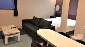 Una habitación de hotel moderna con un sofá negro, una mesita, una cama y un espejo redondo en la pared.