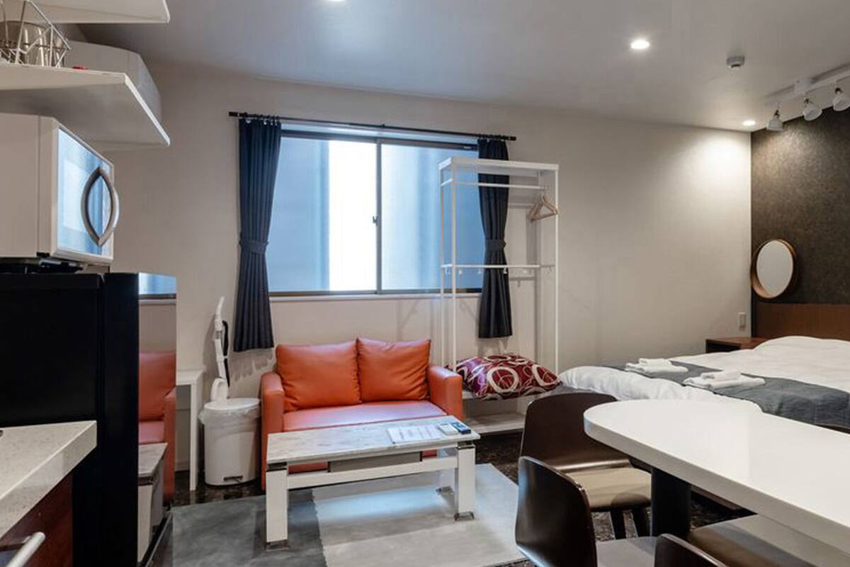 Quarto de hotel com cama, escrivaninha, cadeira, mesa pequena, televisão, janela com cortinas e guarda-roupa.