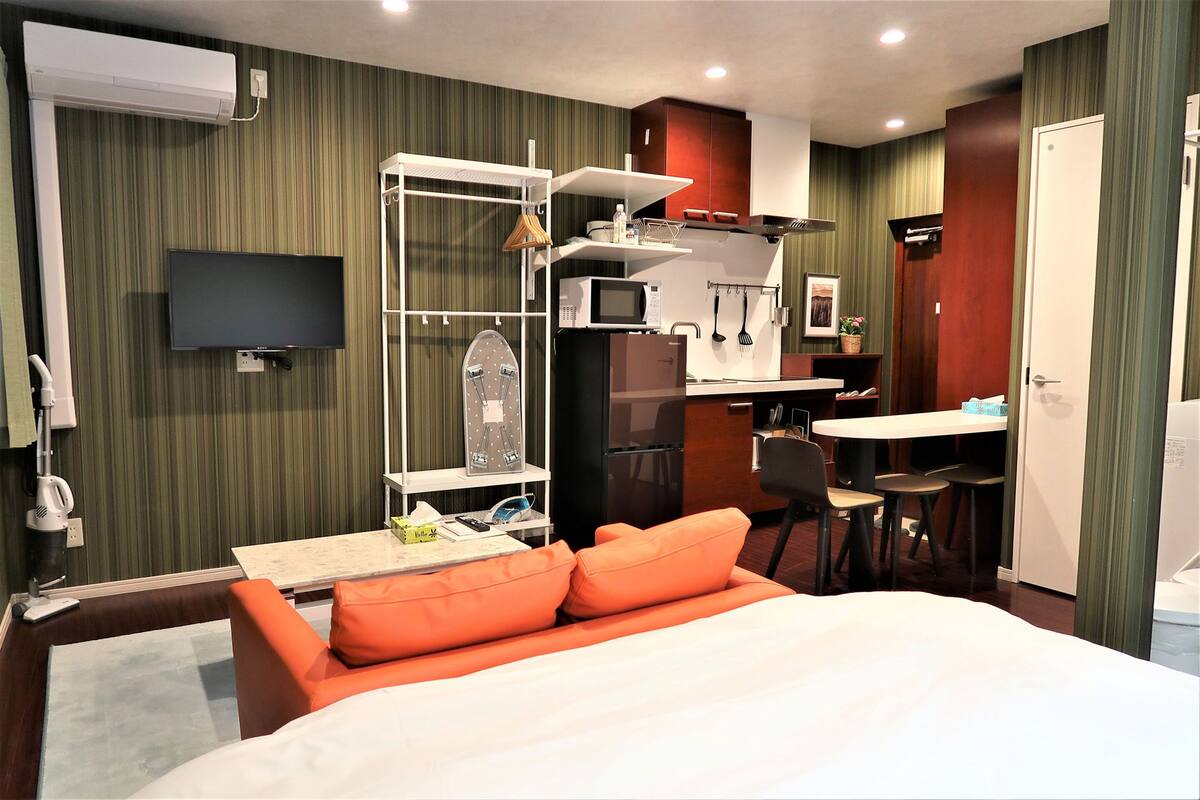 Quarto de hotel com cama, escrivaninha com cadeira, micro-ondas, frigorífico, televisão e uma pequena copa.