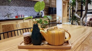 Una mesa de madera con una tetera amarilla, un florero oscuro y un tarro de nueces.