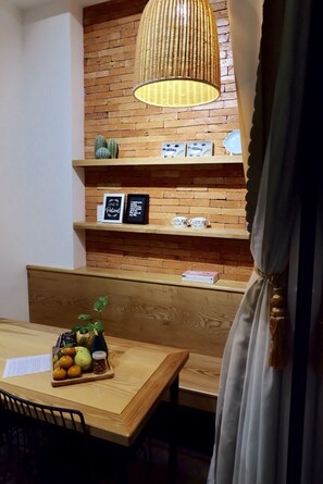 Un comedor acogedor con una mesa de madera, un banco y una pared de ladrillo con estantes que exhiben objetos decorativos y citas enmarcadas.