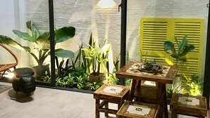 Una habitación con un separador de vidrio, una mesa de madera con sillas y diversas plantas en macetas.