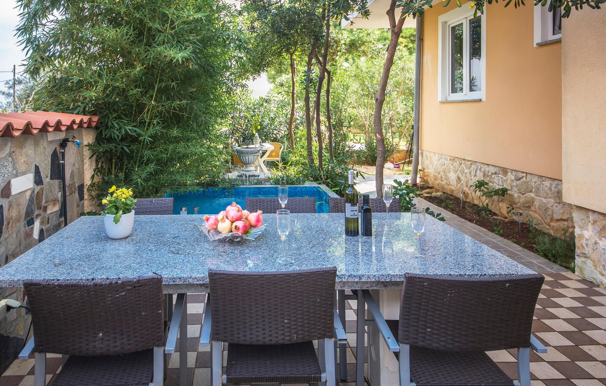 An outdoor dining area with a table and chairs, a fountain, and a pool in the background.