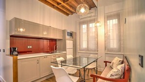 A modern kitchen with a glass dining table and white chairs, a red sofa with floral cushions, and wooden ceiling beams. - DELUX APARTMENT CASA DEL ANILLO TOLEDO (Toledo)