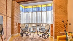 A cozy room with brick walls, a large window with curtains, two rocking chairs, a small table, and a yellow chair. - DELUX APARTMENT CASA DEL ANILLO TOLEDO (Toledo)