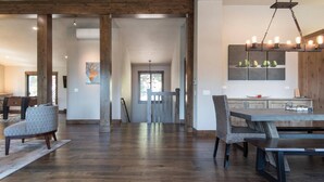 Un vaste espace dédié à la salle à manger, avec une table et des chaises en bois, un luminaire suspendu et, au fond, une vue sur la cuisine.