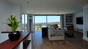 A modern living room with a sofa, a coffee table, and a large window offering a view of the city. - Luxury villa with spectacular sea views, Pvt Pool, Gardens and Parking (Teulada)