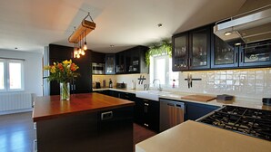 A modern kitchen with dark cabinets, a wooden island, a built-in stove, and a hanging light fixture. - Luxury villa with spectacular sea views, Pvt Pool, Gardens and Parking (Teulada)
