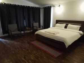 A hotel room with a large bed, two chairs, a wooden floor, and a window with curtains.