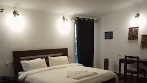 A bedroom with a large bed, a wooden headboard, a bedside table, a chair, and a small table with a lamp. - Asaka Himalayan Inspiration lodge Kasol (Bhuntar)