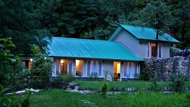 A two-story building with a green roof, surrounded by lush greenery and a stone wall. - Asaka Himalayan Inspiration lodge Kasol (Bhuntar)
