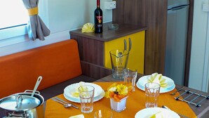 A compact kitchen with a dining area, featuring a table set for four, a wine bottle, and a refrigerator. - Victoria Mobilehome Village Residence Juliamare (Giulianova)