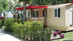 A mobile home with a covered porch, a small deck, and a garden area with shrubs and flowers. - Victoria Mobilehome Village Residence Juliamare (Giulianova)
