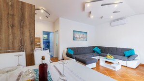 A modern living room with a grey sectional sofa, a white coffee table, and a dining area with a white table set for a meal. - 1 bedroom nice apartment in Pavicini (Pavicini)