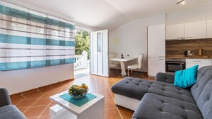 A modern living room with a sofa, a coffee table with fruit, a dining area with a table and chairs, and a kitchen with cabinets and appliances. - 1 bedroom nice apartment in Pavicini (Pavicini)