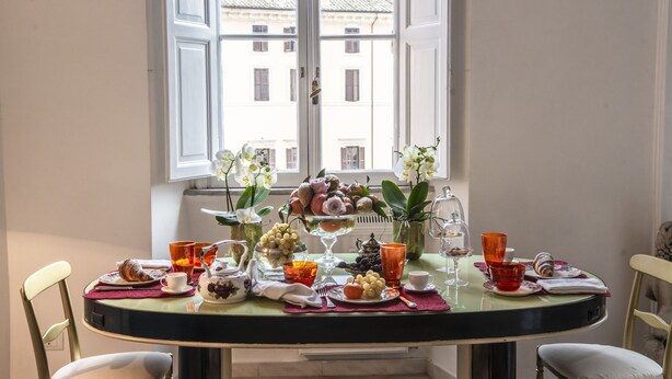 Ein Esstisch, reichhaltig gedeckt mit Früchten, Gläsern und einer Blumenvase.