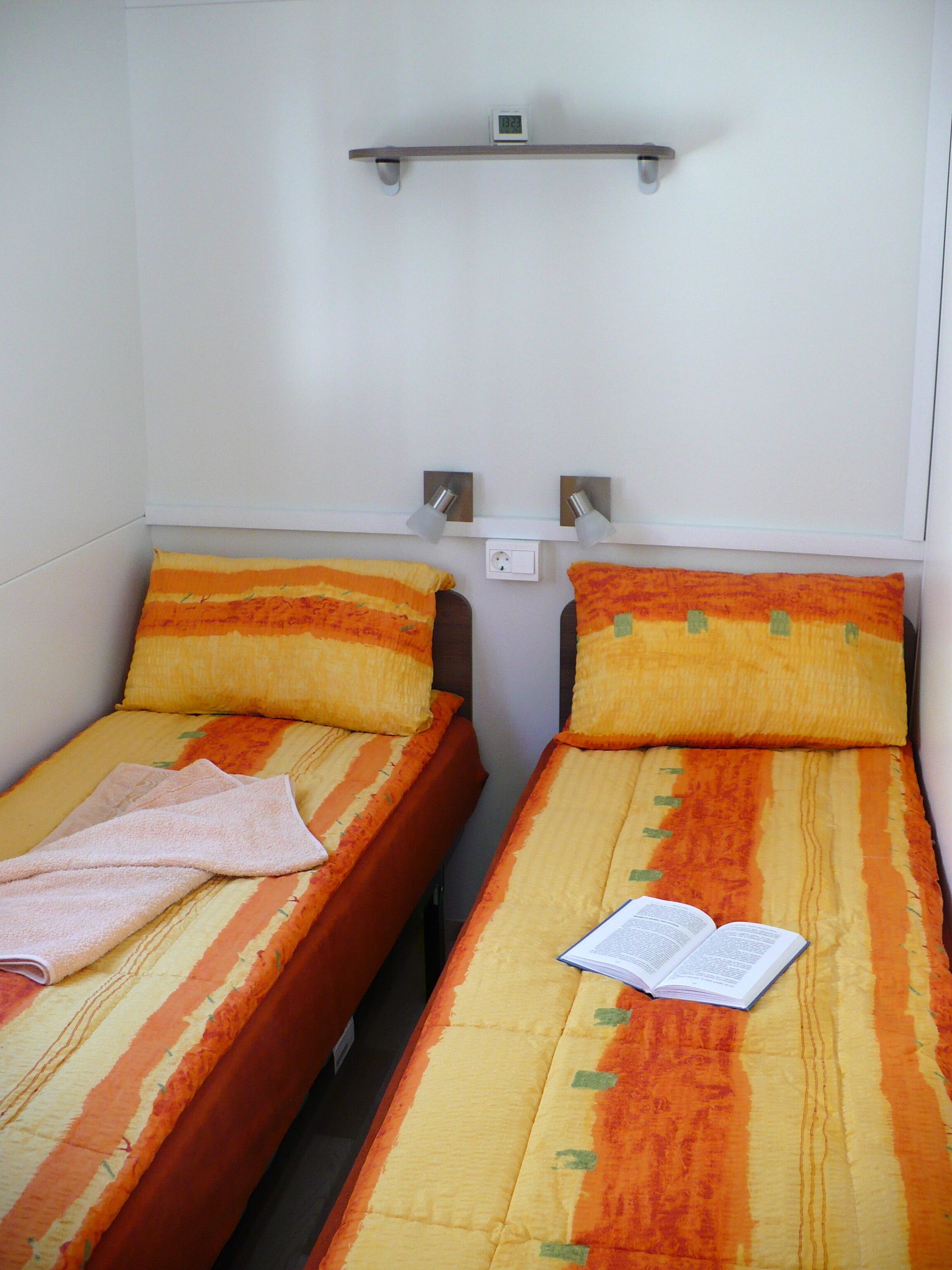 Two single beds with orange and yellow striped bedding, a small shelf above, and a book on one bed.