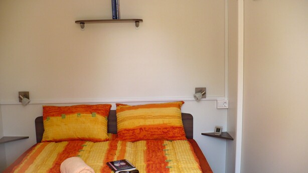 A bed with a striped bedspread, two pillows, a folded towel, and a book with sunglasses on it. - Victoria Mobilehome Tortoreto Lido (Tortoreto)