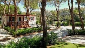A small cabin with a wooden deck, surrounded by lush greenery and trees. - Victoria Mobilehome Tortoreto Lido (Tortoreto)