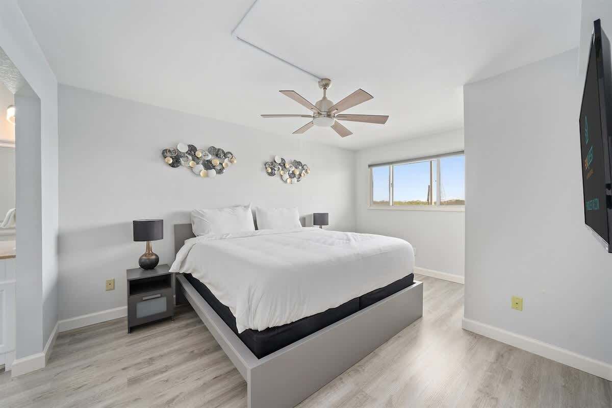 Une chambre moderne avec un grand lit, un ventilateur de plafond et des œuvres d’art décoratives au mur.