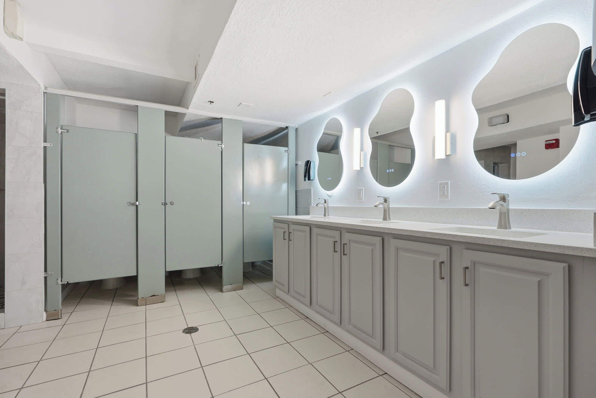 A modern bathroom with a large vanity, multiple sinks, and a mirror with circular lighting.