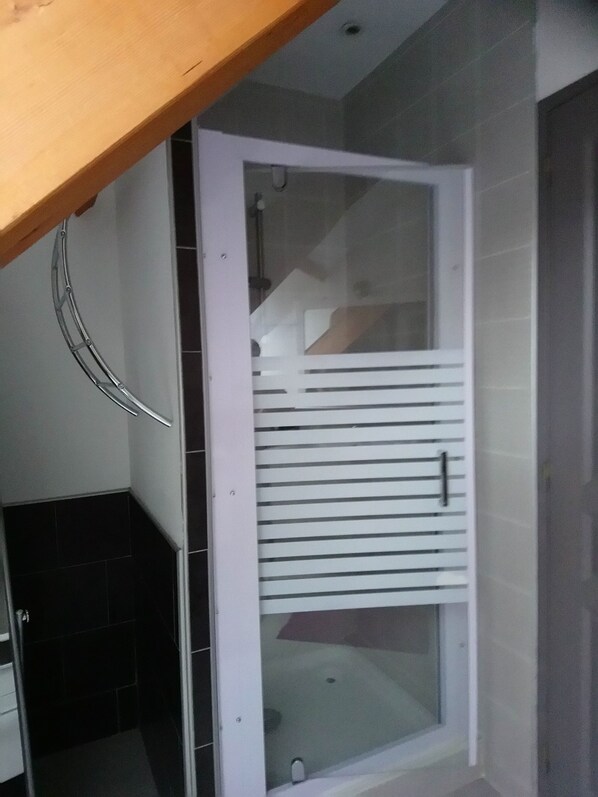 A bathroom with a glass shower enclosure, a white door, and a tiled floor.