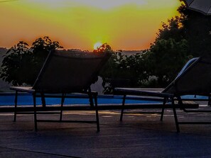 A sunset view with two lounge chairs facing a pool.