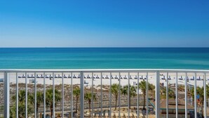 A beach view with a white fence, palm trees, and beach umbrellas.