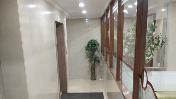 A clean, well-lit hallway with a tiled floor, a potted plant, and a wooden railing. - Hotel Prime (Ahmedabad)