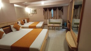 A hotel room with two beds, a sofa, a small table, and a mirror. - Hotel Prime (Ahmedabad)