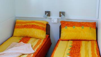 Two single beds with orange and yellow striped bedding, a small shelf above, and a book on the right bed.