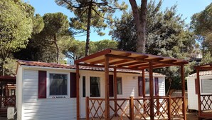 Ein kleines, eingeschossiges Mobilheim mit einer Holzterrasse und einer überdachten Veranda.