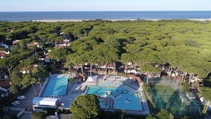 Luftaufnahme eines Küstenresorts mit zwei Swimmingpools, einem Wasserpark und einem Strand im Hintergrund.