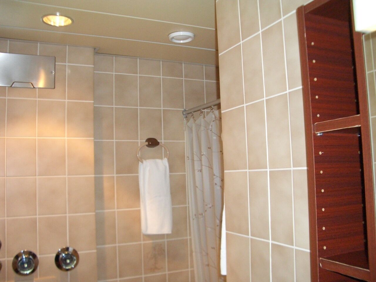A bathroom with beige tiles, a white towel hanging on a metal rack, a wooden cabinet, and a shower curtain.