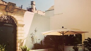 Eine Terrasse mit Tisch und Stühlen unter einem großen Sonnenschirm, umgeben von Kübelpflanzen und einer Steinmauer.