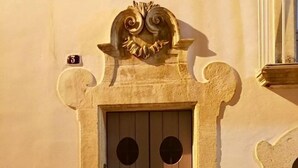 Ein steinerner Durchgang mit verziertem Bogen, zwei Holztüren mit runden Aussparungen und ein kleines Regal darüber.