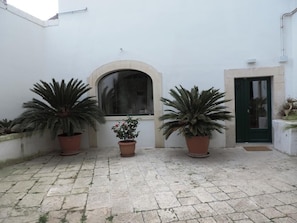 A courtyard with three large potted plants, a window, and a door. - Casa Adele - Dimora del 1700 nel centro storico (Martina Franca)