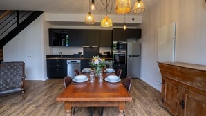 Zona pranzo con tavolo in legno apparecchiata per quattro, una sedia in pelle scura e una cucina moderna sullo sfondo.