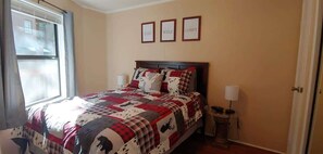 A bedroom with a bed, a window, a bedside table, and a wall with framed text.